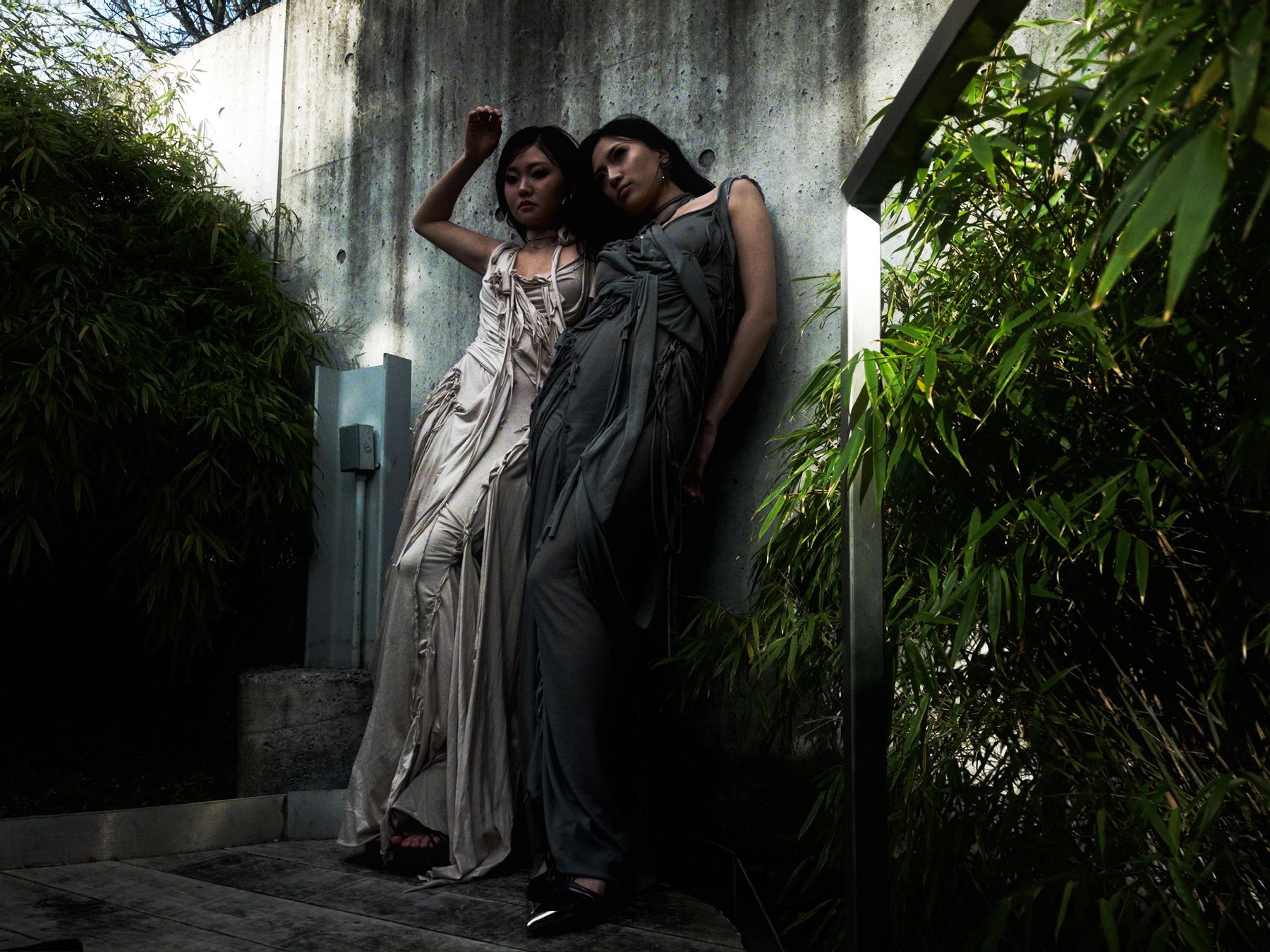 Two women in long dresses against a garden wall
