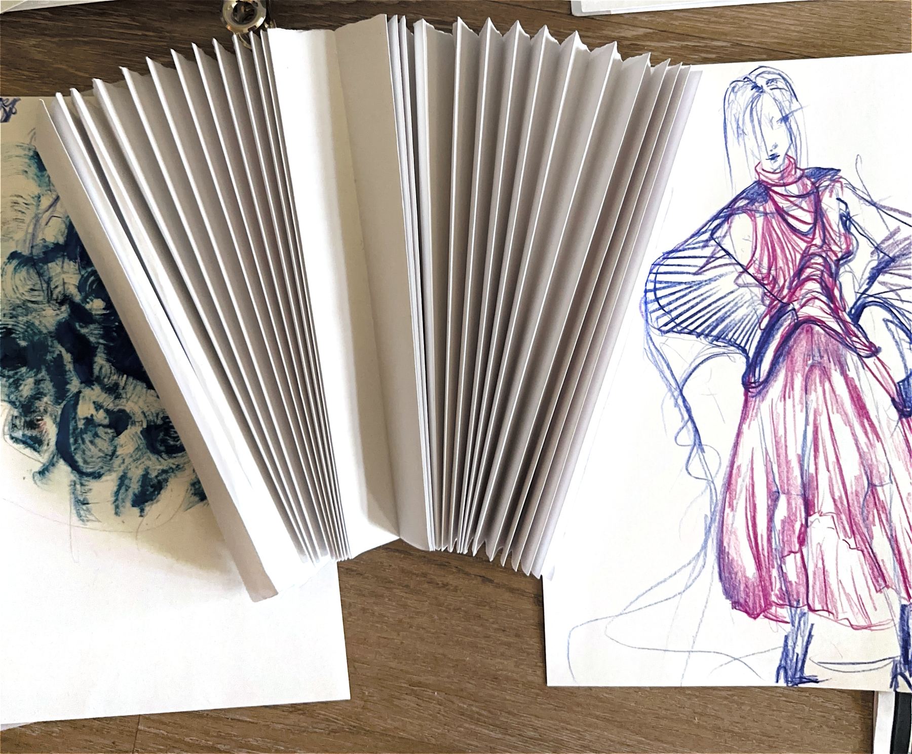 Pleated paper fan beside a pink gown sketch
